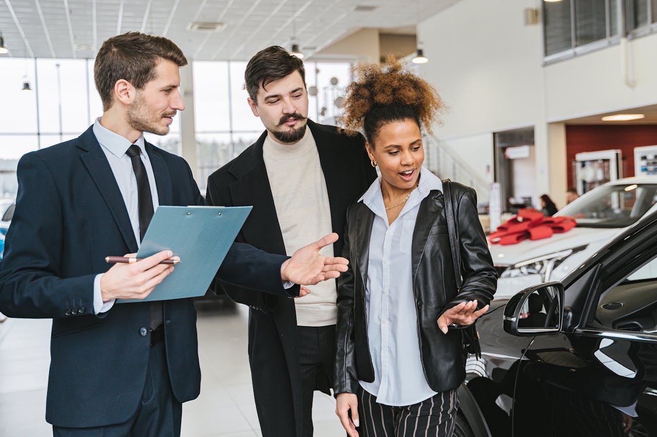 A diverse group of adults discussing vehicles at a bright modern car dealership.